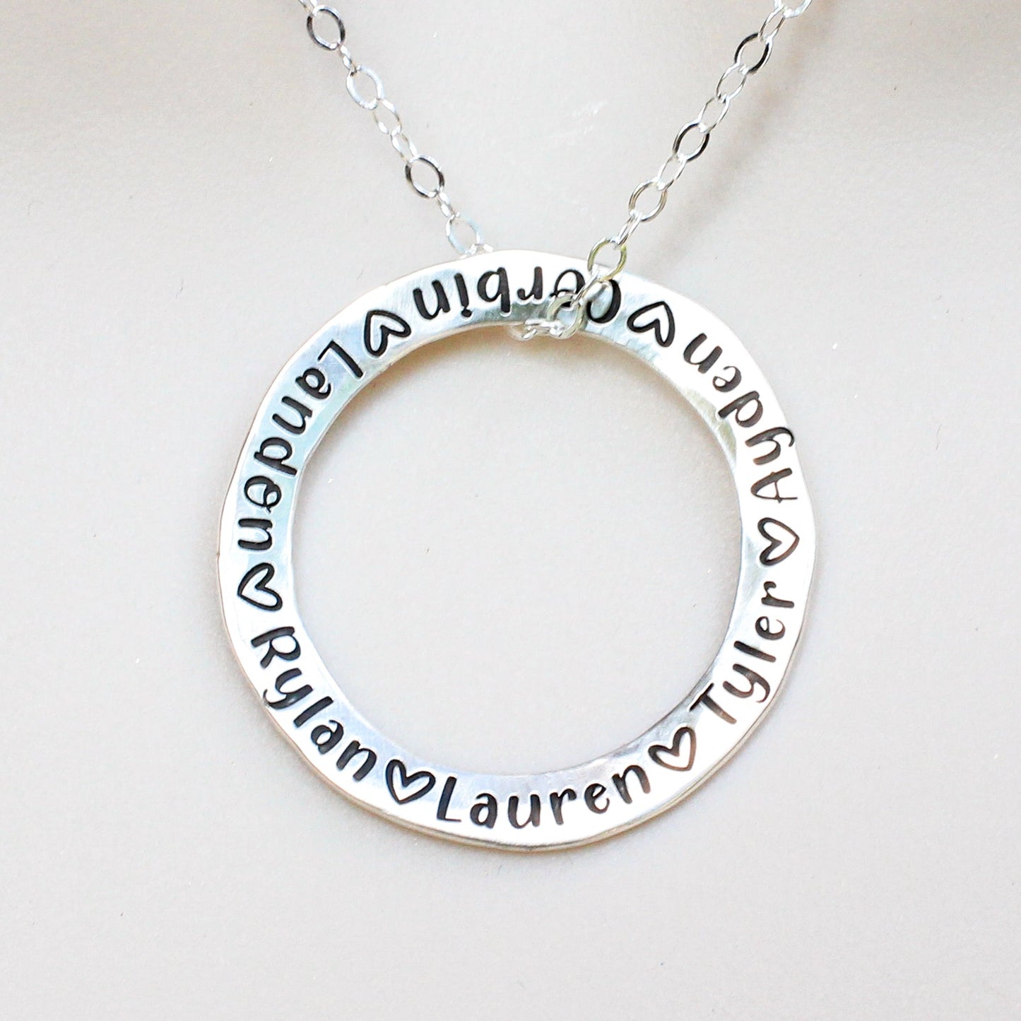 Silver necklace with circular pendant engraved with names on a white background
