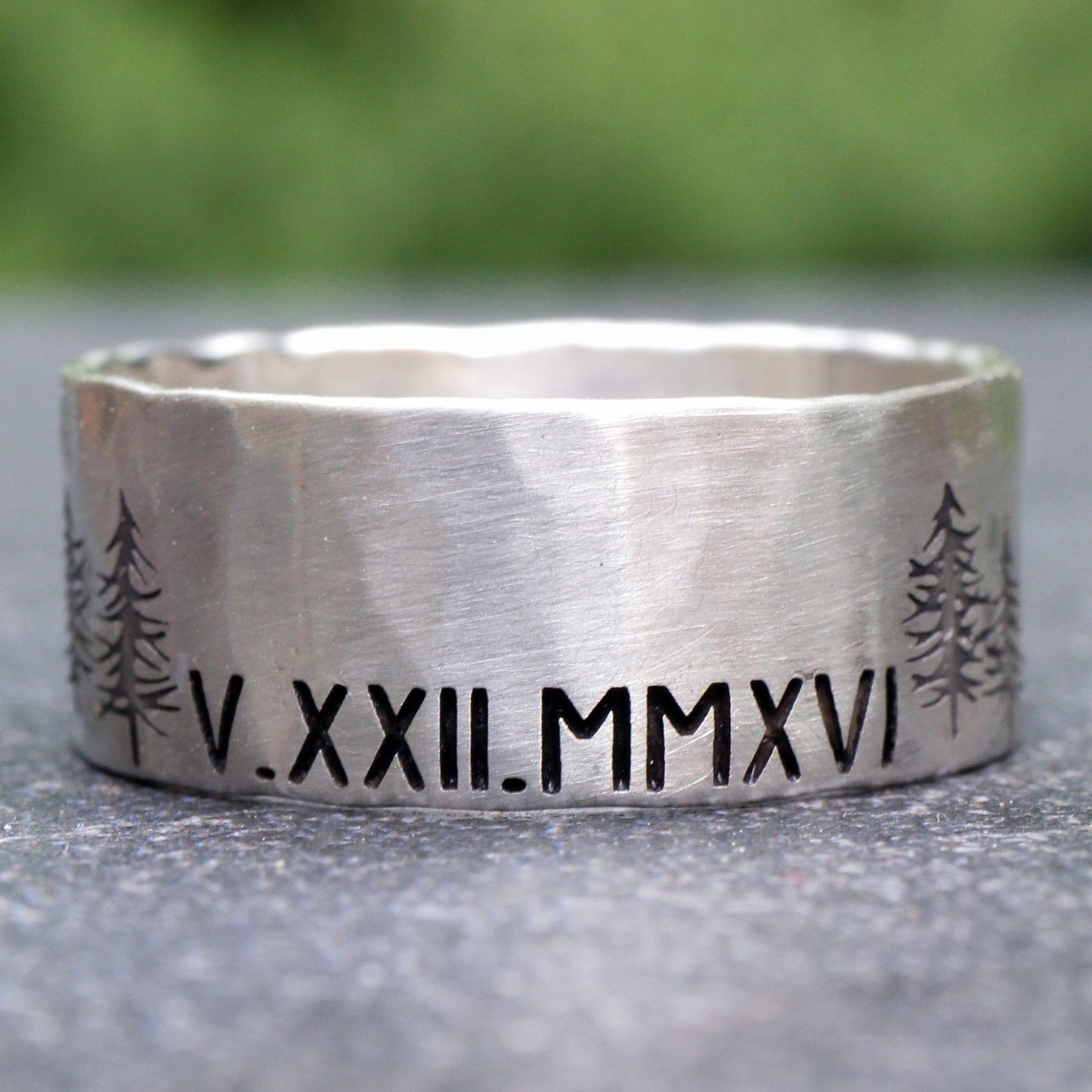 Silver ring with engraved Roman numerals and tree designs on a blurred natural background