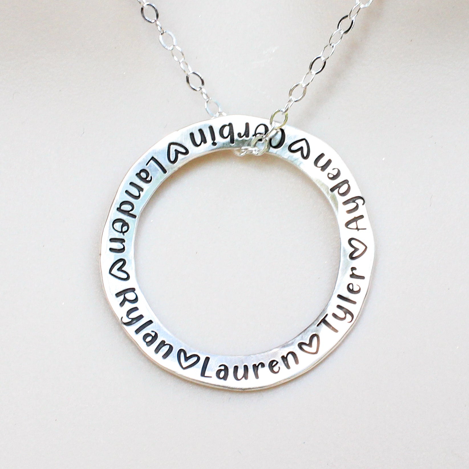 Silver necklace with circular pendant engraved with names on a white background